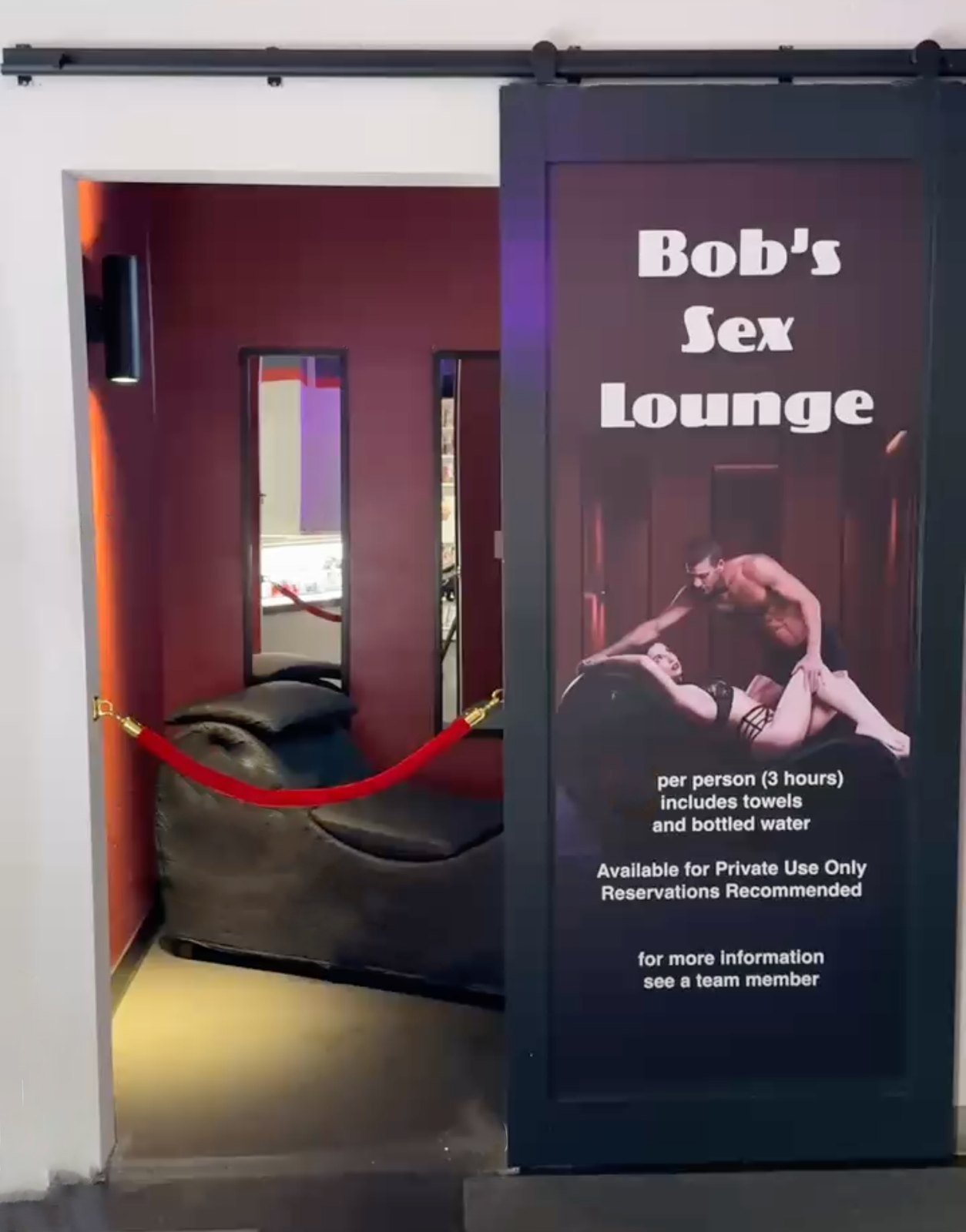 The entrance to Bob's Sex Lounge: a sliding door with the room's sign, beside the open doorway showing a red-walled room with a lounge seat behind a velvet rope